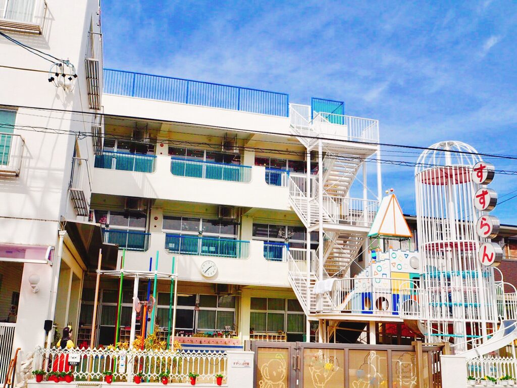 晴れた日に撮影された、すずらん幼児園の園舎と遊具のある園庭の様子。外観にはカラフルなすべり台と「すずらん」の看板が見える。