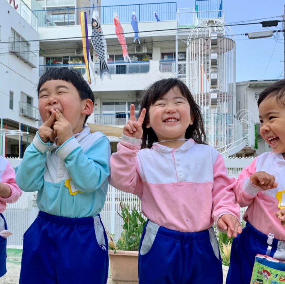 すずらん幼児園の園庭で元気いっぱいに笑う4人の子どもたち。仲良く並んで楽しそうに過ごす春の日の一コマ。