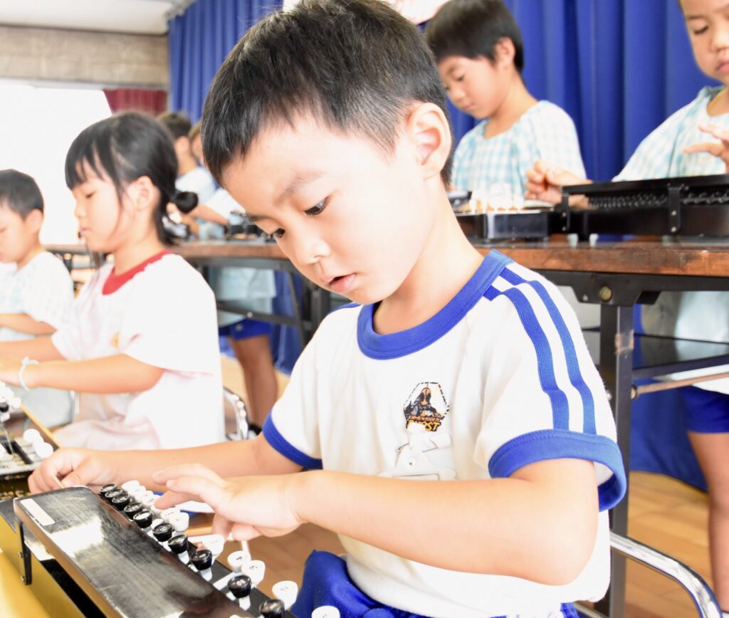 幼稚園の音楽の時間に、子どもたちが木琴を使ってリズム練習をしている様子。真剣な表情で演奏に取り組んでいる。