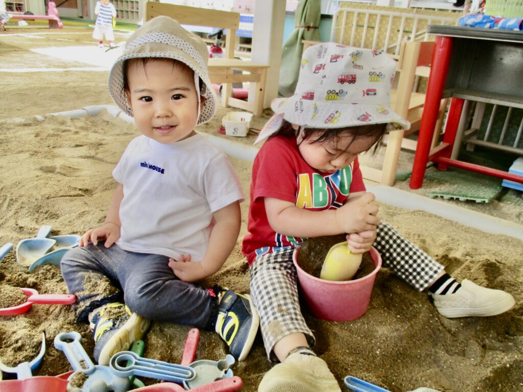 すずらん幼児園の砂場で、スコップやバケツを使って遊ぶ小さな子どもたち。好奇心いっぱいの表情が印象的。