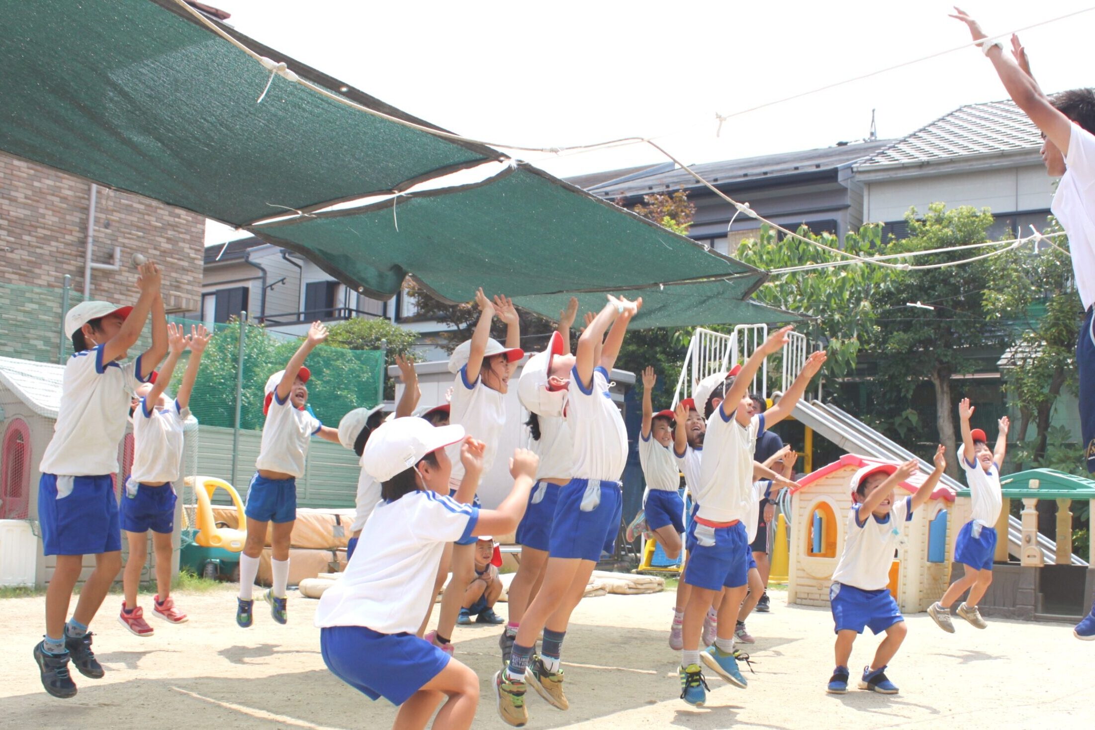 すずらん幼児園の園庭で、先生と一緒にジャンプ運動を楽しむ子どもたちの様子。元気いっぱいの体操風景。