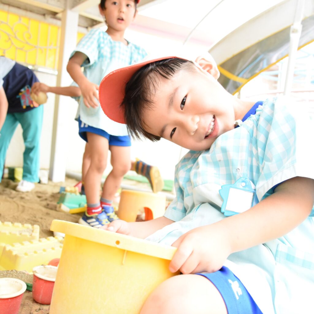 すずらん幼児園の砂場で遊ぶ子どもたち。笑顔いっぱいでバケツや型を使って砂遊びを楽しんでいる様子。