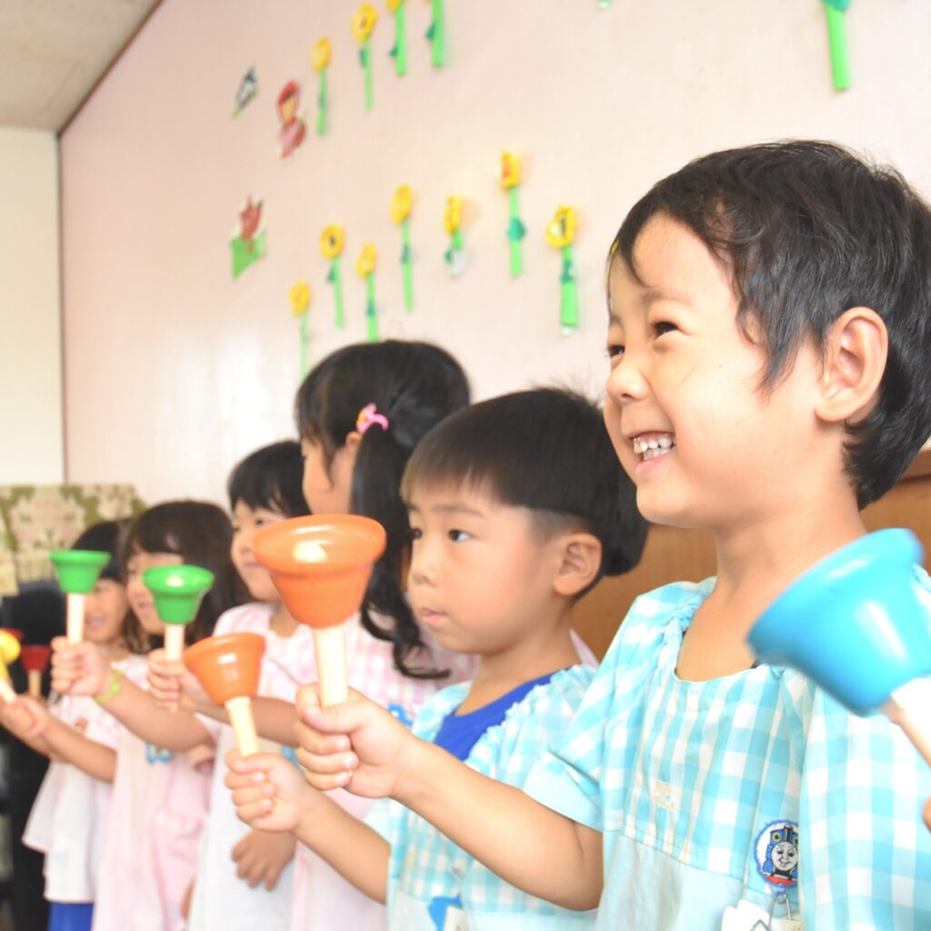すずらん幼児園の教室で、ハンドベルを持って音楽活動を楽しむ子どもたち。明るく元気な雰囲気。